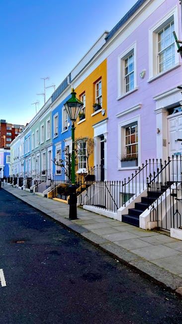 Image of a row of colorful, pastel-painted terraced houses on a residential street, featuring blue, yellow, and lavender facades. Each house has white-framed windows and small front gardens with decor